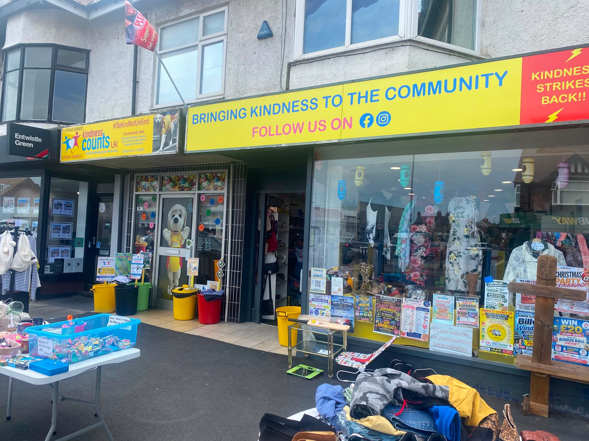 The charity shop window, full of clothes and posters for the charity's events, with the Nic mascot costume standing in the doorway.