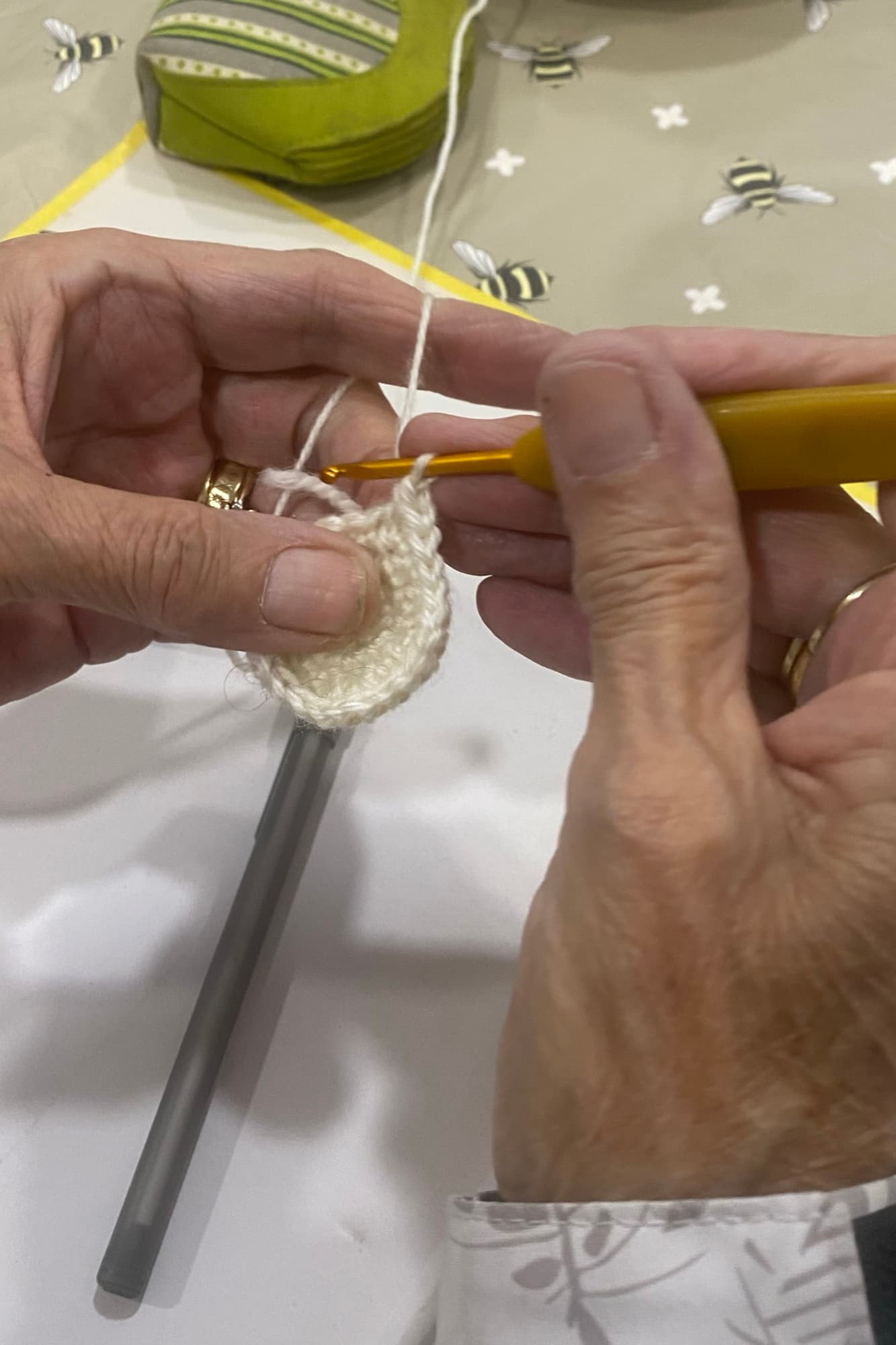 Close-up of hands crocheting with a yellow hook at crochet club, a pattern sheet on the table.