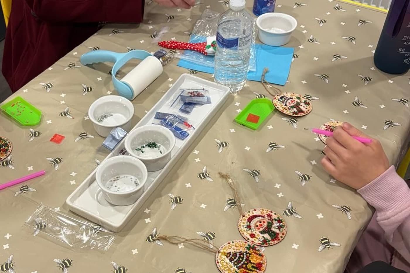 Diamond art at the hub — finished snowman and Christmas tree decorations beside trays of coloured gems and an applicator pen.