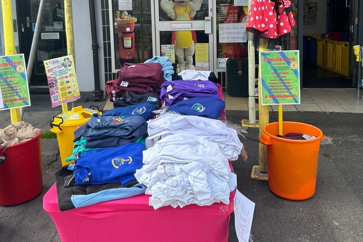 Donated school uniform sorted into piles on a table outside the hub, beside the collection buckets and the posters listing what the charity is collecting.