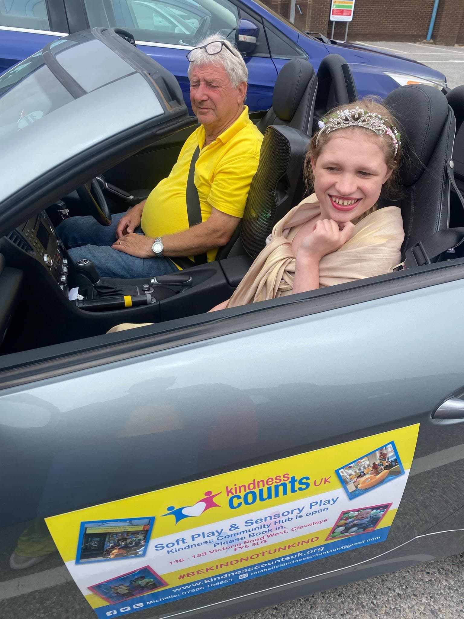 A young carnival princess in a tiara riding in the Kindness Counts UK car.
