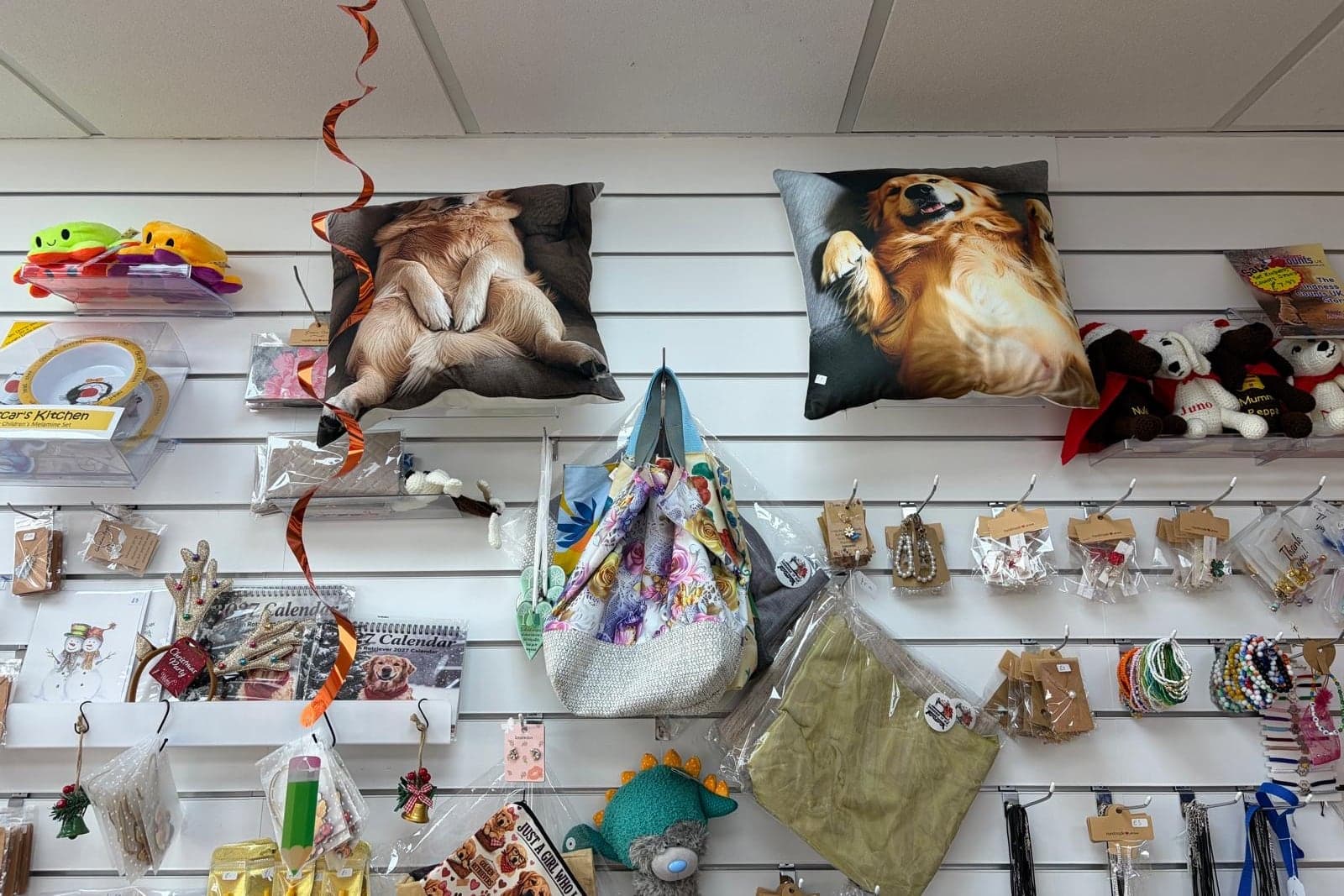 Handmade jewellery, bags and crocheted toys on the gift shop wall, under two dog cushions.