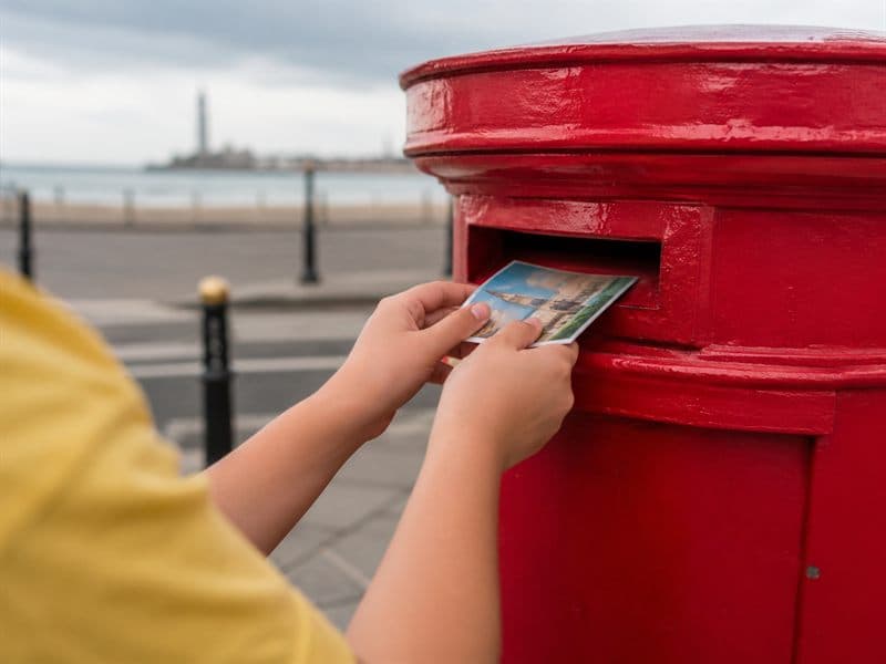 A child's hands posting a kindness postcard into a brightly painted box.