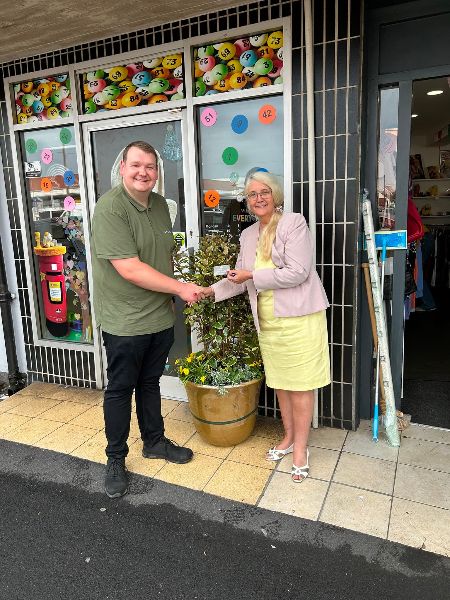 A member of The Plant Place team shaking hands with Kindness Counts UK outside the charity shop, beside one of the new planters.