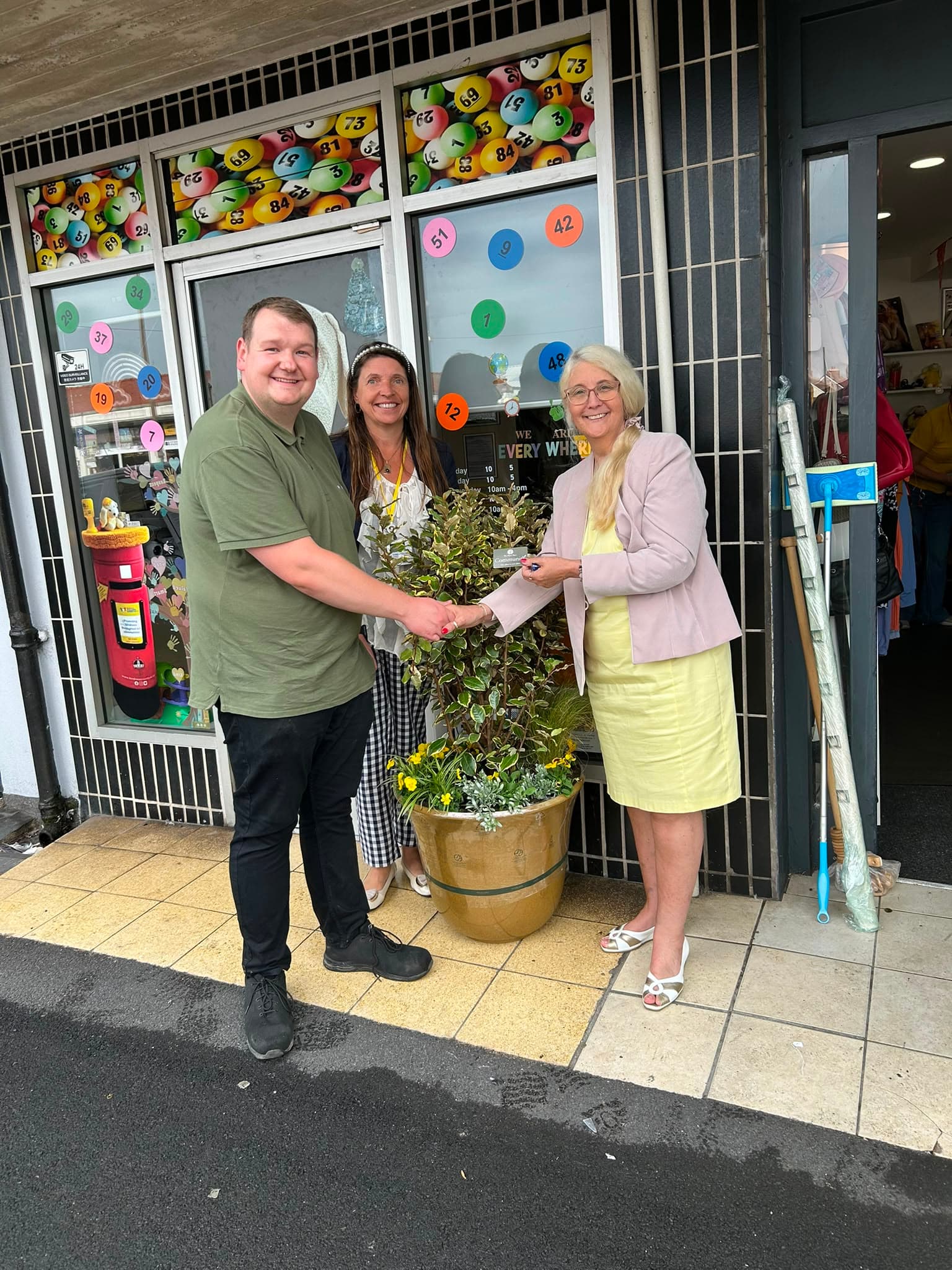 Three people outside the charity shop with one of the donated planters.
